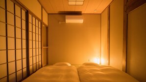 Une pièce de style japonais traditionnel, avec un sol recouvert de tatamis, un paravent coulissant de type shoji et un lit équipé d’un futon.