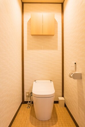 A compact, modern bathroom with a toilet, a small trash bin, and a wall-mounted toilet paper holder. - HARUKIYA Hanare (Osaka)