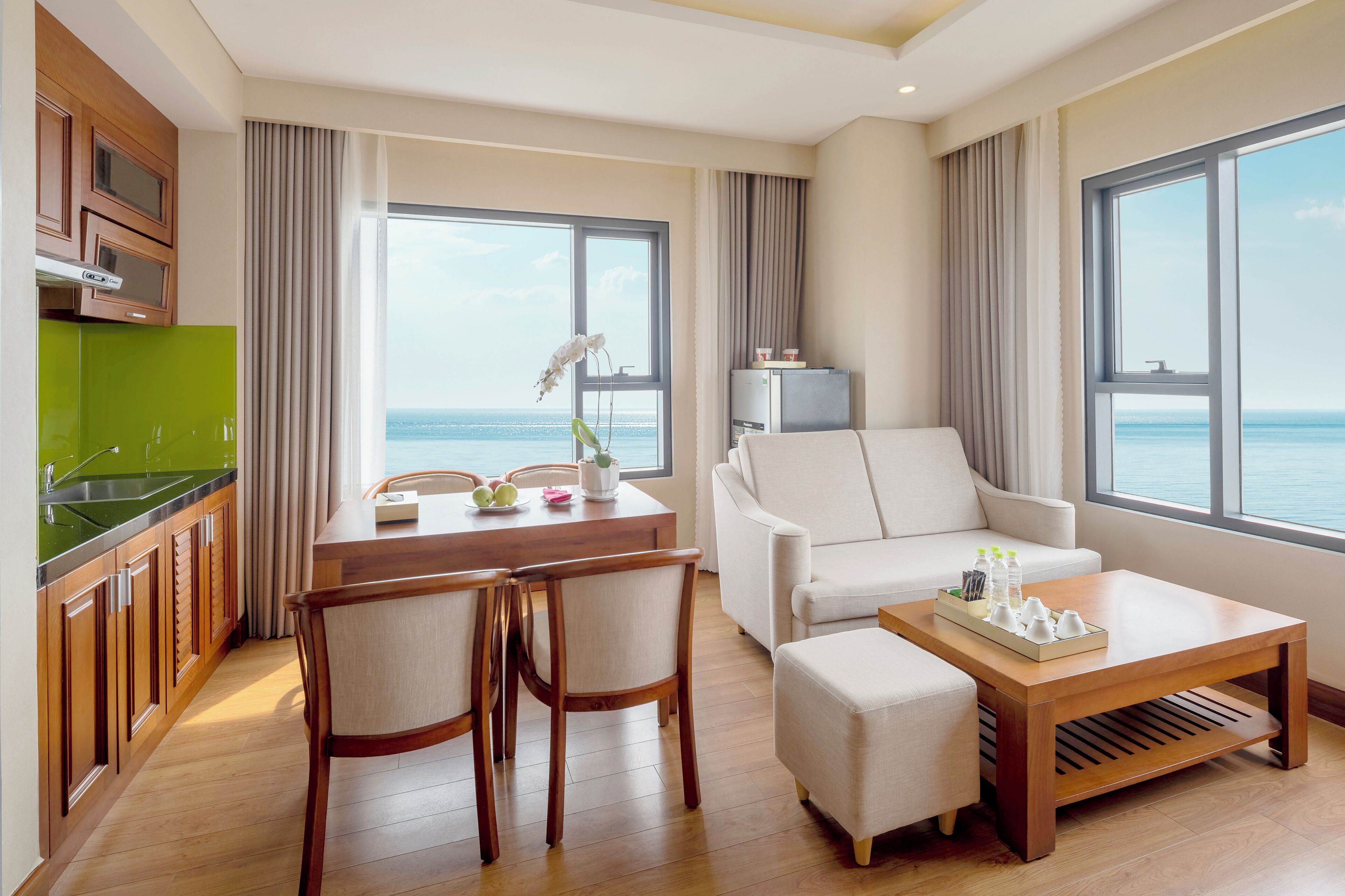 A modern hotel room with a dining area, a sofa, and a view of the sea.