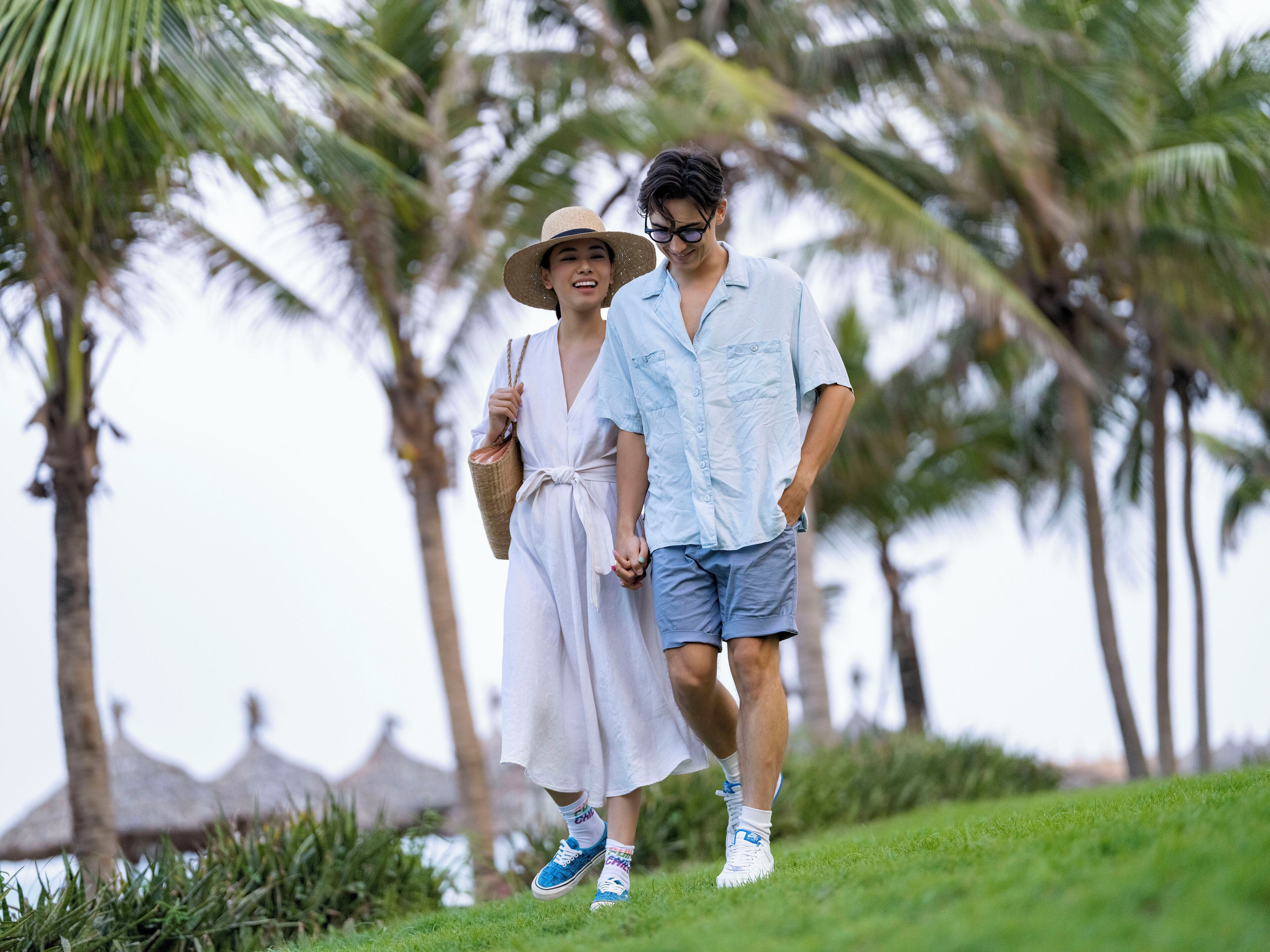 A couple walking on a grassy path with palm trees in the background.