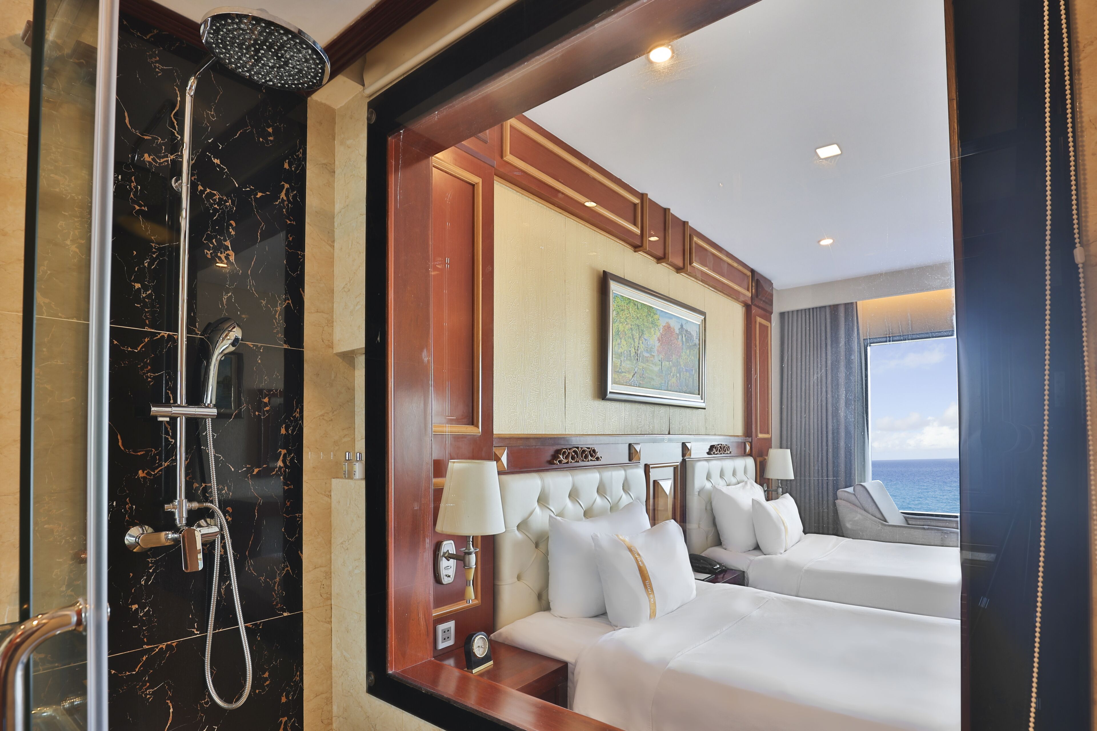 A hotel room with a marble shower, two beds, a large window with a view, and a framed picture on the wall.