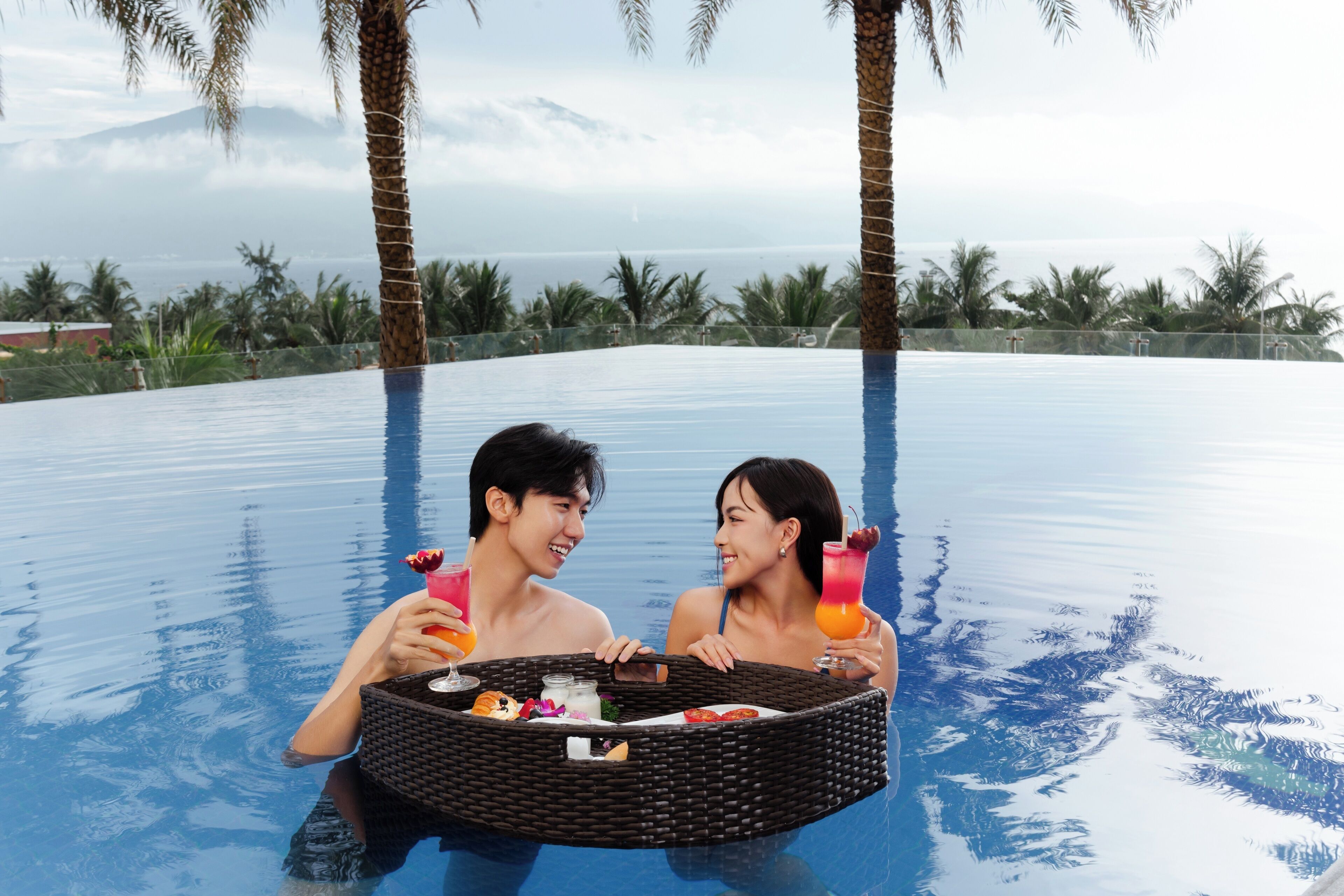 A couple in a swimming pool with a wicker basket containing food and drinks.