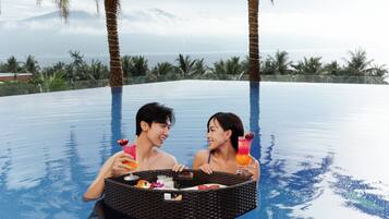 A couple in a swimming pool with a wicker basket containing food and drinks.
