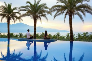 Two people meditating on an infinity pool with palm trees and a mountain view. - DLG Hotel Danang (Da Nang)