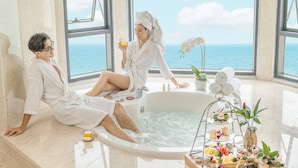 A luxurious spa room with a large bathtub, a tray of snacks, and a view of the sea. - DLG Hotel Danang (Da Nang)