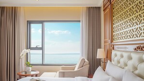 A hotel room with a large window, a bed, a chair, and a small table with a lamp. - DLG Hotel Danang (Da Nang)