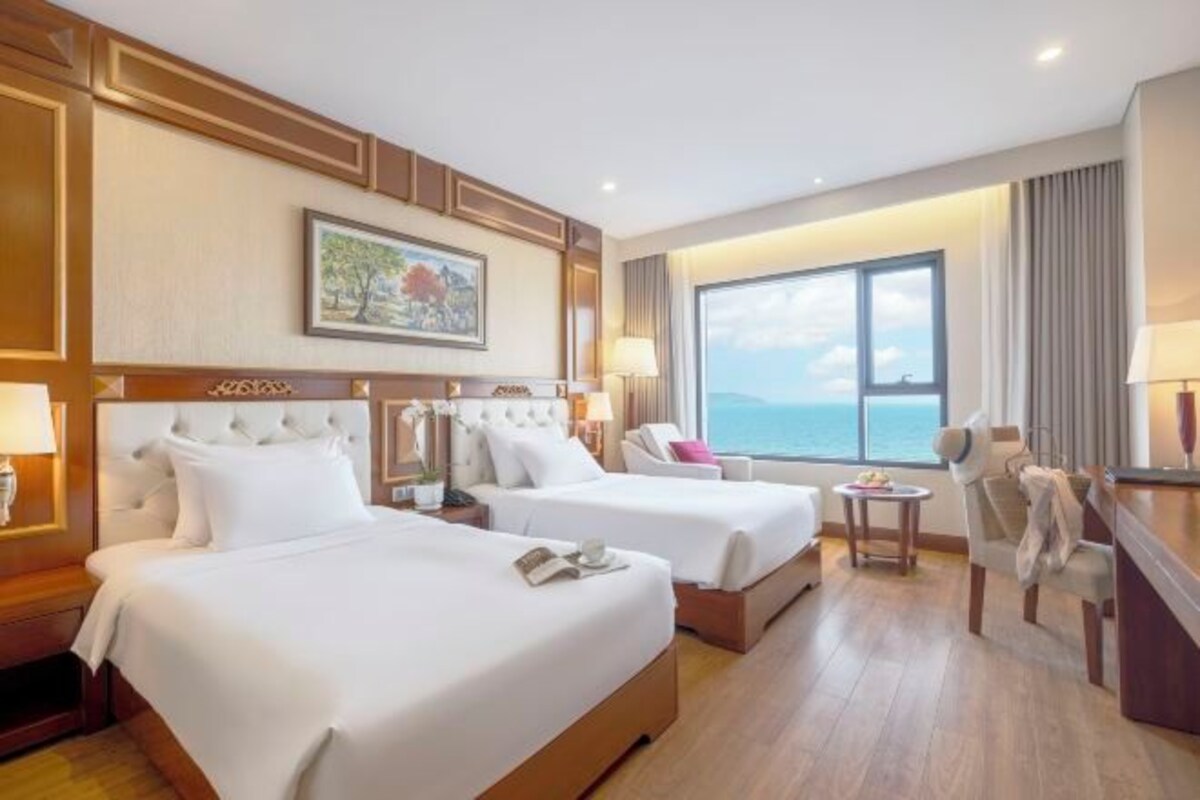 Une chambre d’hôtel avec deux lits, un bureau, une chaise, une petite table et une grande fenêtre donnant sur un beau paysage.