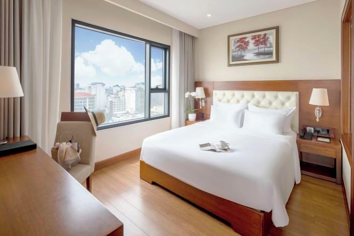 Une chambre d’hôtel avec une grande fenêtre, un lit, un bureau et une chaise.