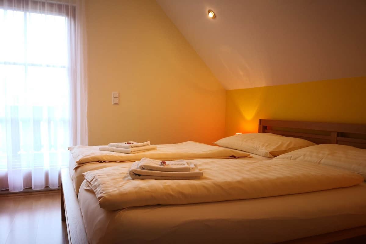 Une chambre avec deux lits, une fenêtre avec des rideaux légers et une lampe fixée au mur.