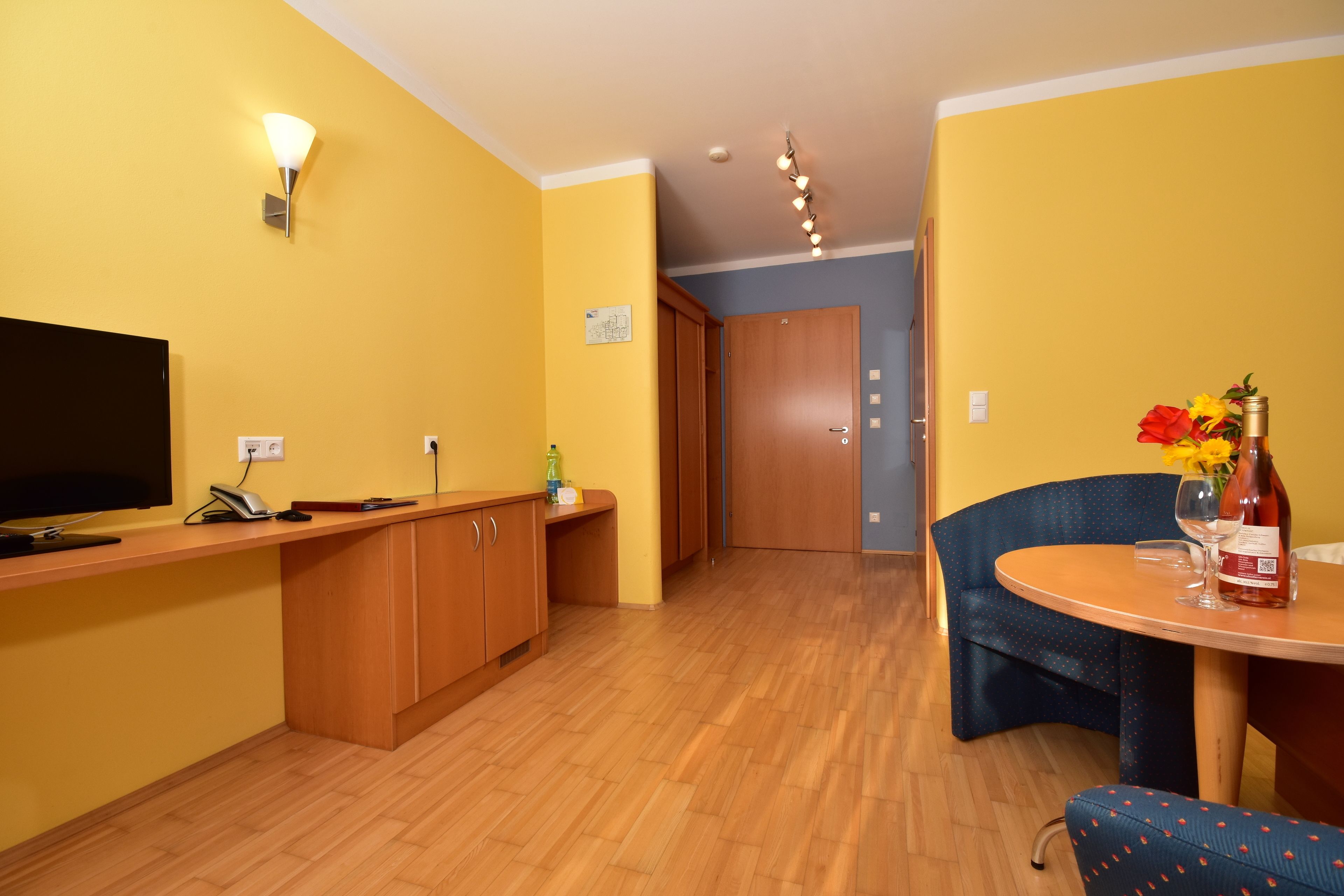 A compact living space with a kitchen area, a dining table with chairs, a TV, and a wall-mounted light fixture.