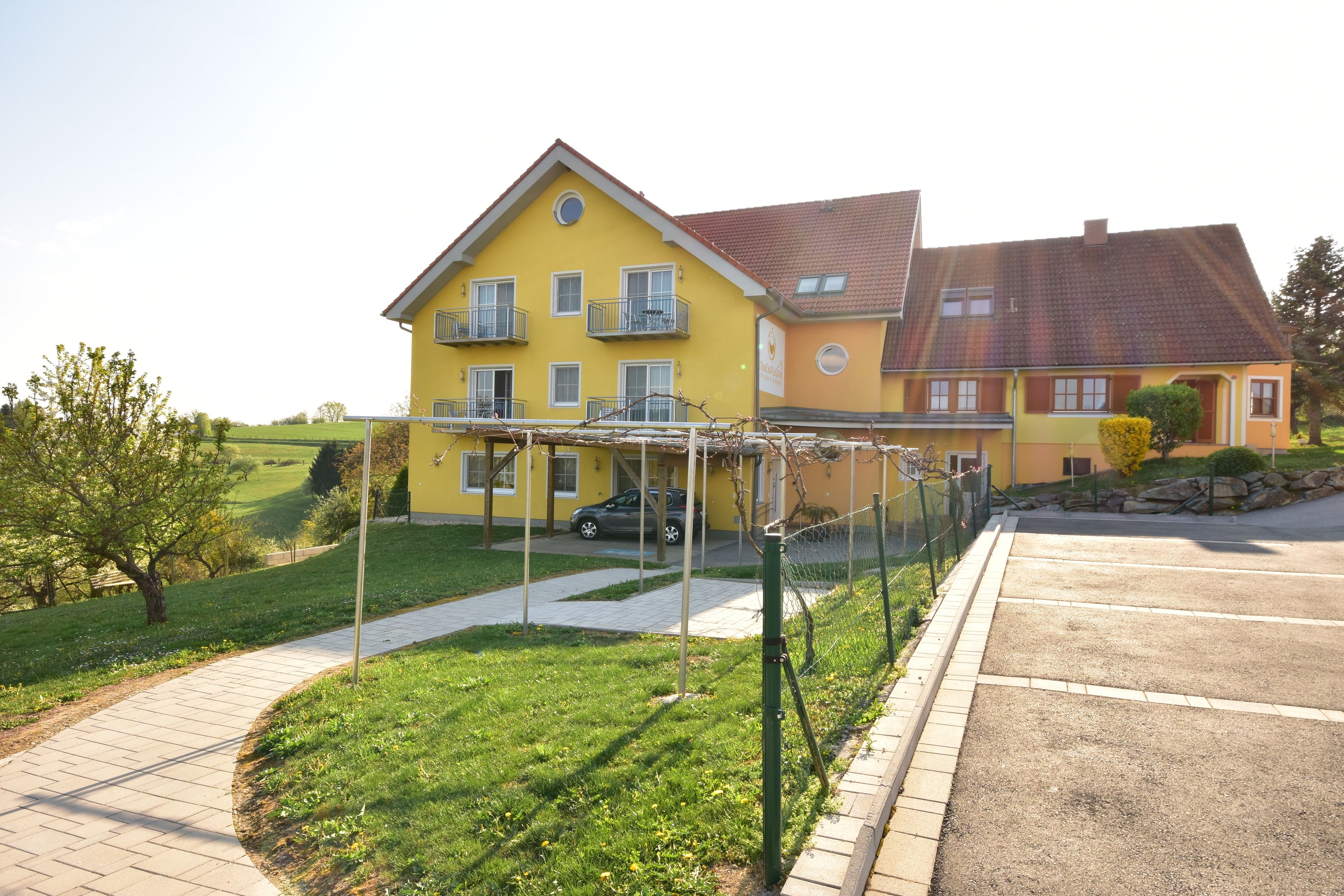 A yellow building with a paved driveway and a fenced garden area.