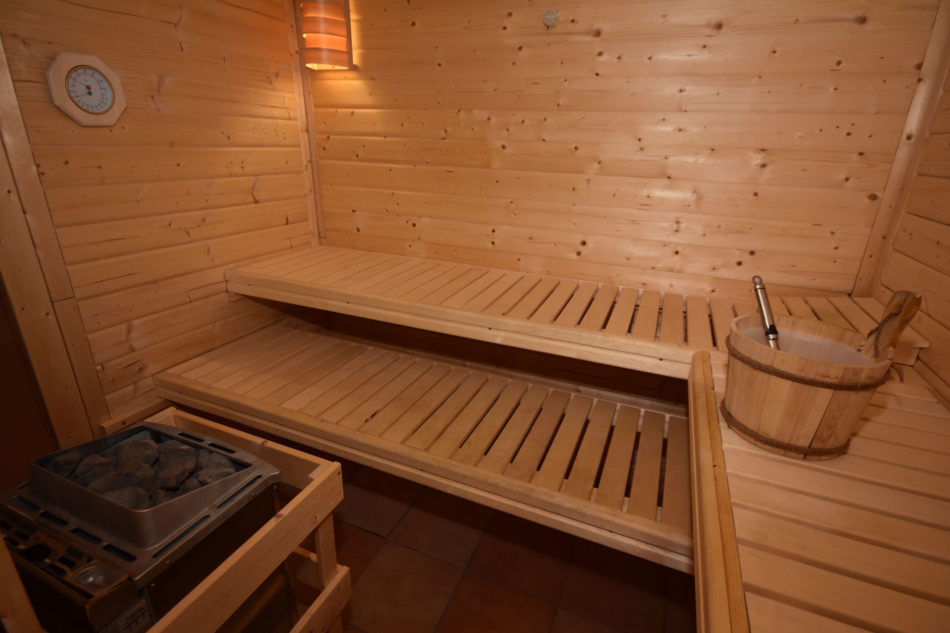 Una sauna de madera con bancos, un balde de madera y un calentador de sauna.