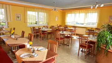 A dining area with multiple tables and chairs, yellow walls, and large windows with curtains.