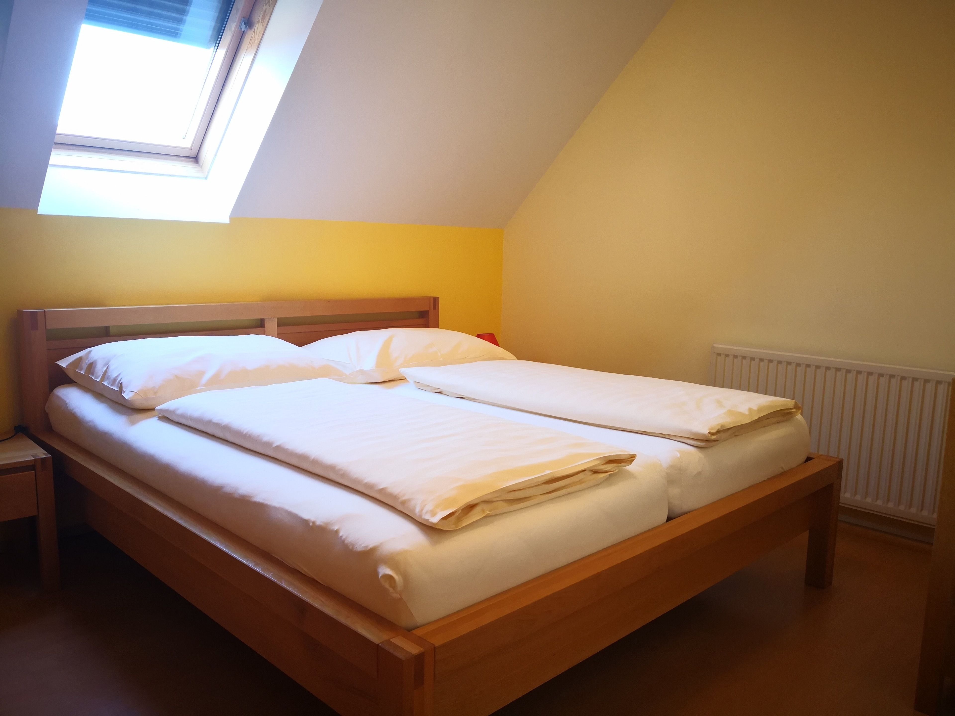 A single bed with a wooden frame and white bedding in a room with yellow walls and a skylight.