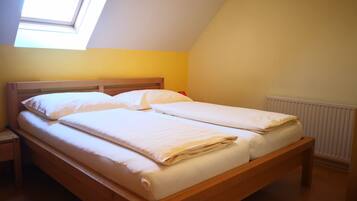 A single bed with a wooden frame and white bedding in a room with yellow walls and a skylight.