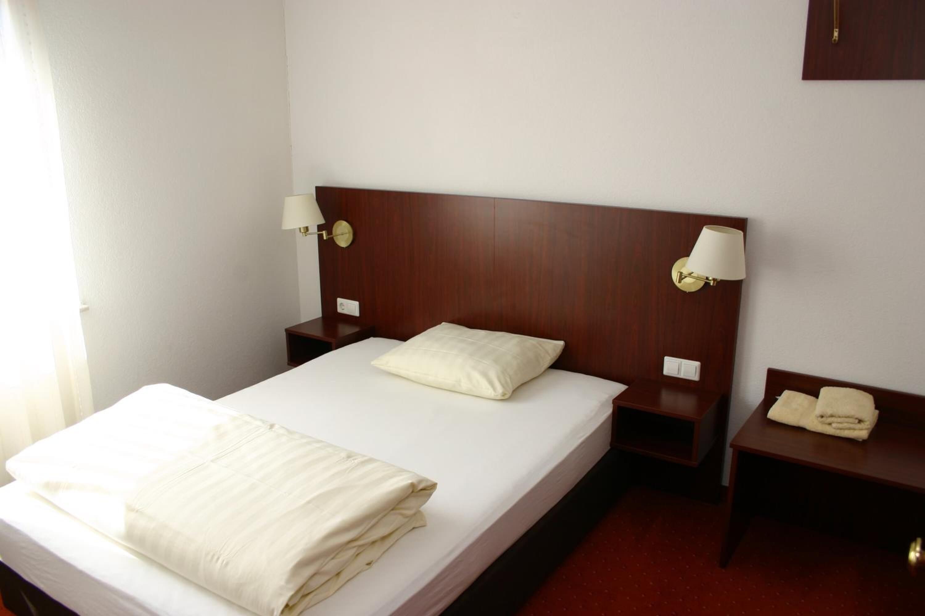 A hotel room with a single bed, two bedside tables, a wooden headboard, and two wall-mounted lamps.