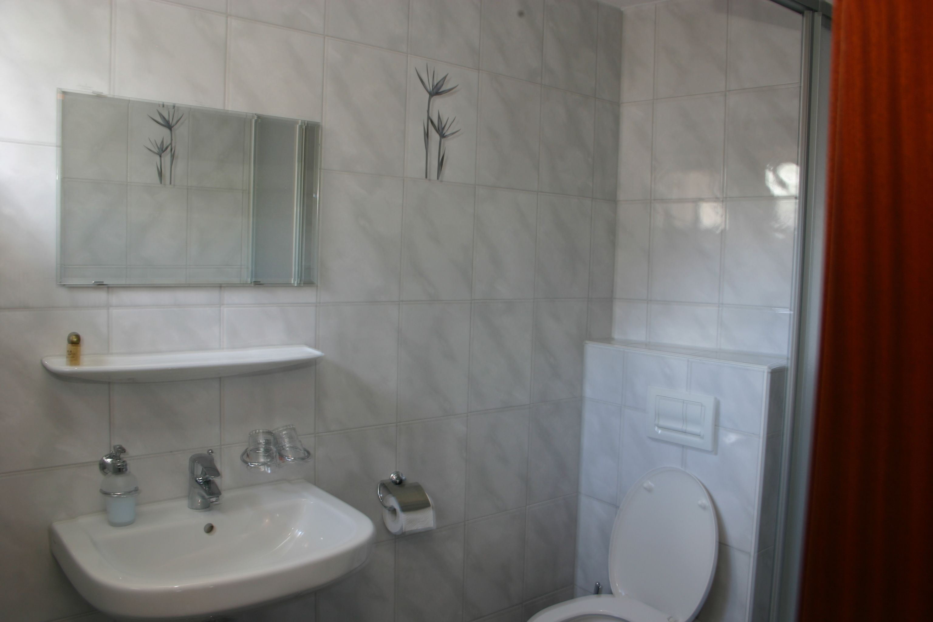 A bathroom with a sink, mirror, toilet, and a shower area.