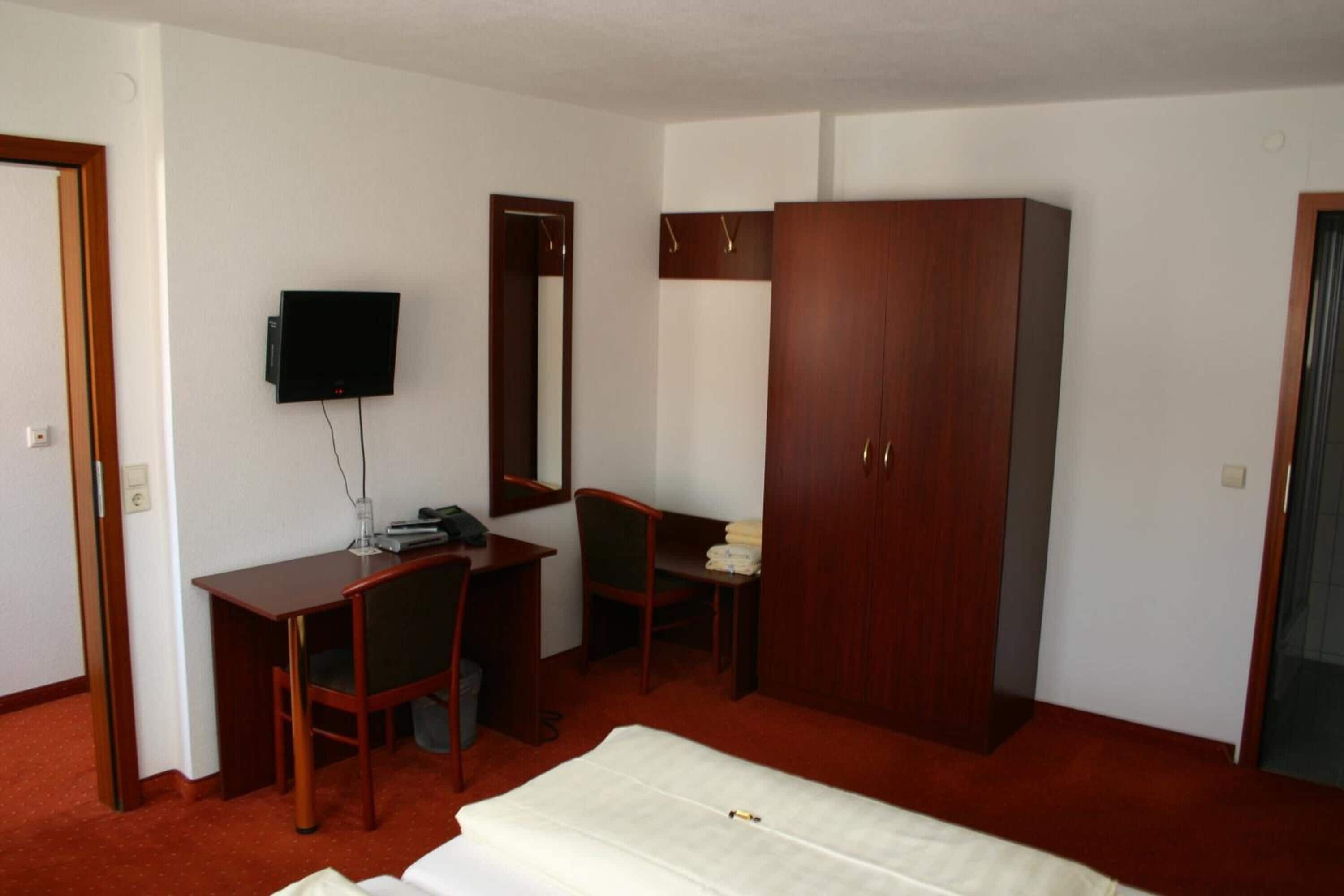 A hotel room with a bed, a desk, a chair, a wardrobe, and a television.