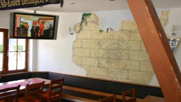 A restaurant interior with a television mounted on the wall, wooden tables and benches, and a mural on the wall.