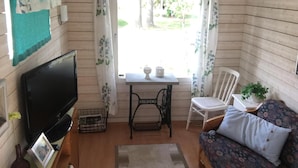 A cozy room with a television, a small table with two white containers, a white chair, a sofa with patterned cushions, and a window with curtains. - ♥ Seaside cottage ♥ Boat fishing snowmobile running (Luleå Ö)