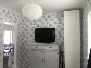 Huoneessa on televisio, joka on sijoitettu kaappiin, ruokailutila, jossa on tuoleja ja pöytä, sekä ovi.
