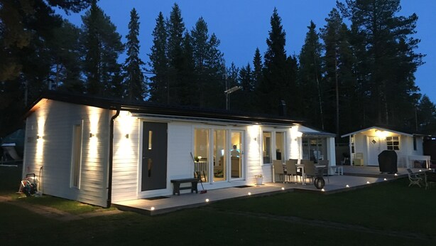 A two-story cabin with a porch, large windows, and a well-lit exterior. - ♥ Seaside cottage ♥ Boat fishing snowmobile running (Luleå Ö)