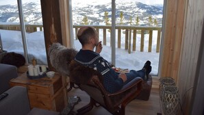 Eine Person sitzt am Fenster mit Blick auf schneebedeckte Berge.