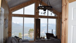 Ein gemütliches Zimmer mit großem Fenster und herrlicher Aussicht auf Berge und einen See. Es gibt ein Sofa und eine Holzbalkendecke.