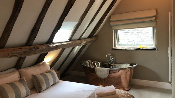 A bedroom with a sloped ceiling, a large window, a bathtub, and a bed with pillows. - Galtres Lodge Hotel (York)