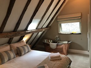 A bedroom with a sloped ceiling, a large window, a bathtub, and a bed with pillows.