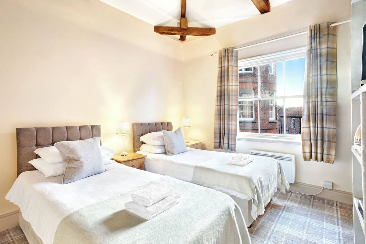A hotel room with two beds, a window with curtains, and a view of buildings outside.