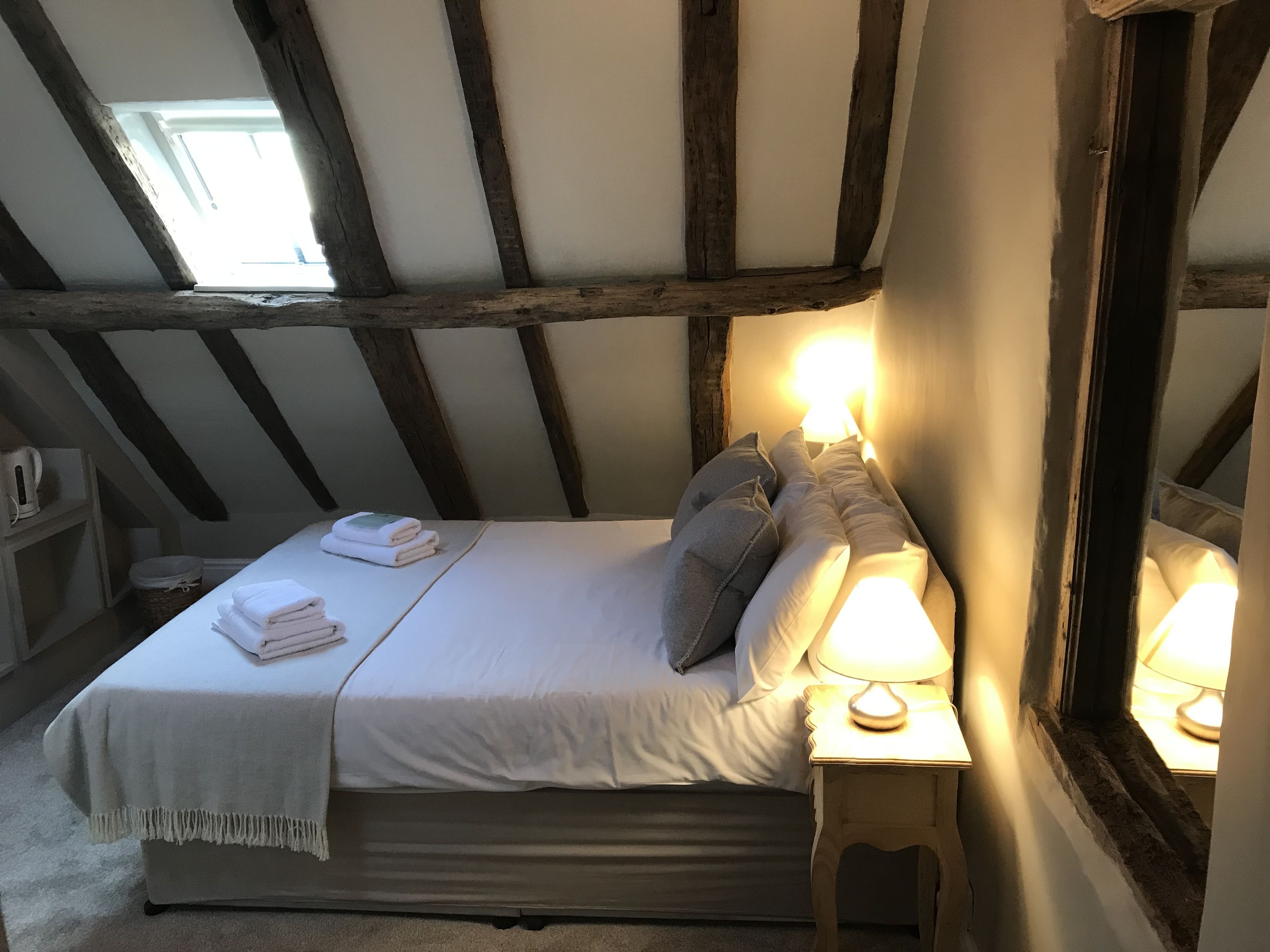 A bedroom with a bed, bedside lamps, a window, and a wooden ceiling structure.