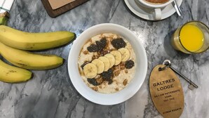 A breakfast setting with a menu, a bottle of champagne, a cup of coffee, a bowl of oatmeal with bananas and berries, a glass of orange juice, and a key with a hotel tag. - Galtres Lodge Hotel (York)