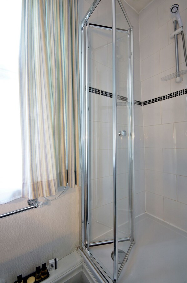 A glass-enclosed shower with a chrome frame, white tiled walls, and a striped curtain.