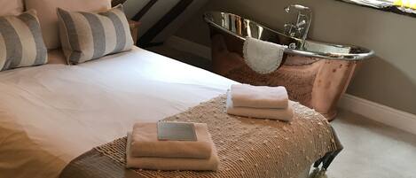 A bedroom with a large bed, a wooden ceiling, a bathtub, and a window.