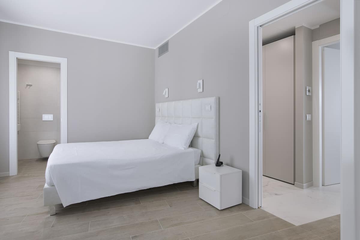 A modern bedroom with a bed, bedside table, and a door leading to another room.