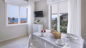 Un coin repas avec une table mise pour le petit-déjeuner, un téléviseur fixé au mur et un balcon avec vue sur la mer.