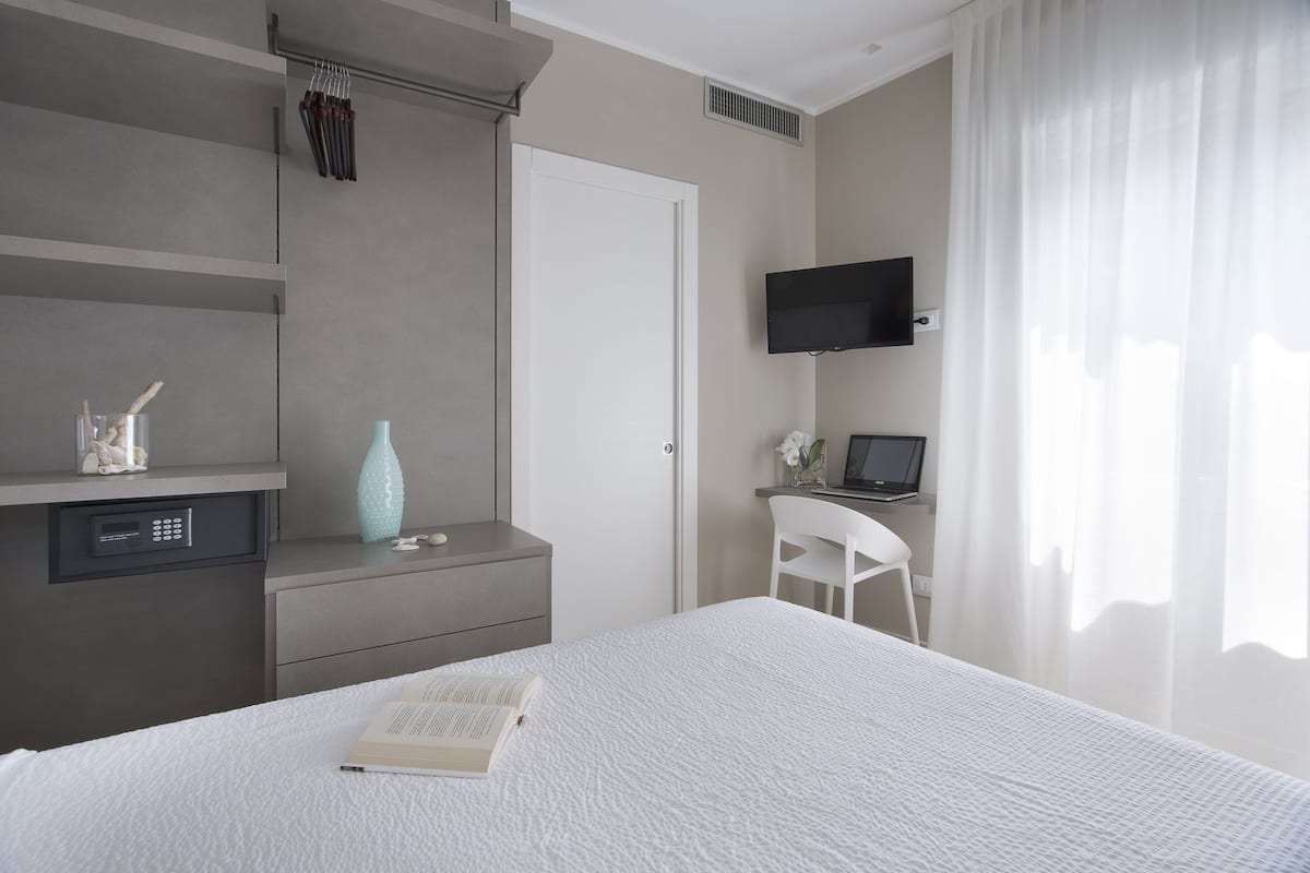 A modern bedroom with a bed, a desk with a laptop, a TV, and a chair.