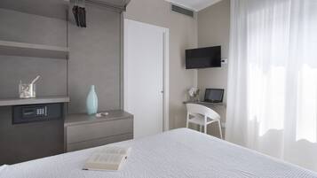 Ein modernes Schlafzimmer mit Bett, Schreibtisch, Laptop, Fernseher und Stuhl.