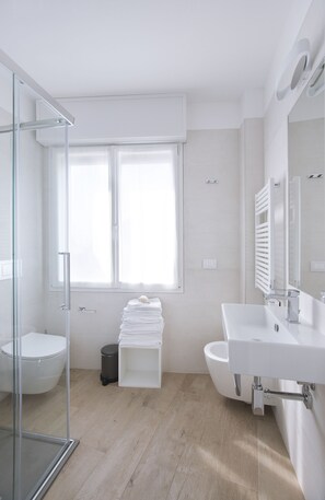 A modern bathroom with a glass shower enclosure, a toilet, a sink, and a large window providing natural light. - Residence Dolcemare (Laigueglia)