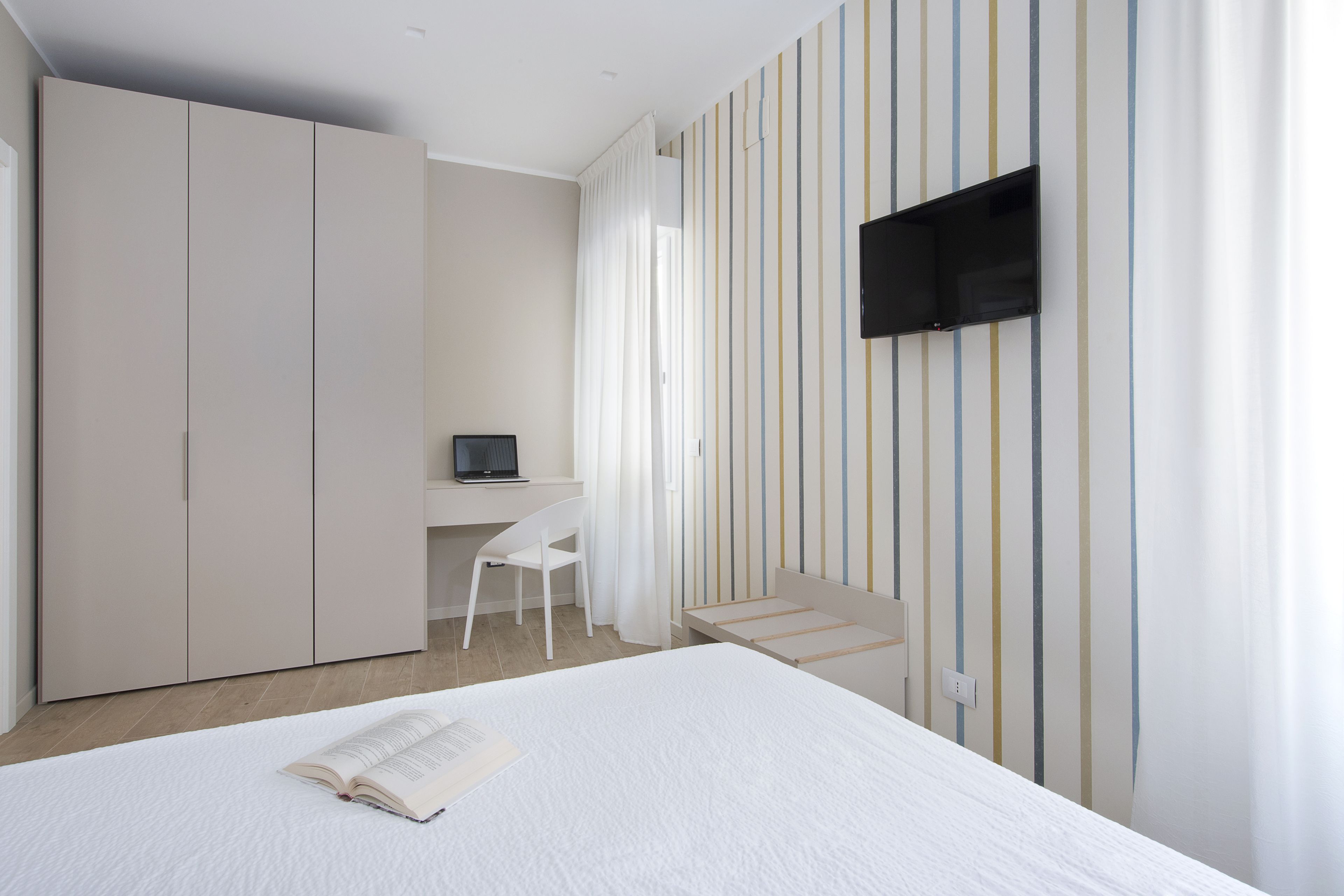 A bedroom with a bed, a desk, a chair, and a TV mounted on the wall.