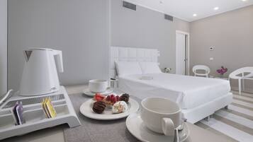 Quarto de hotel com uma cama, uma máquina de café, uma bandeja com pastéis e uma chávena sobre uma mesa.