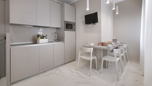 Une cuisine moderne avec des meubles gris, un four à micro-ondes encastré et un coin repas avec des chaises blanches et une table.