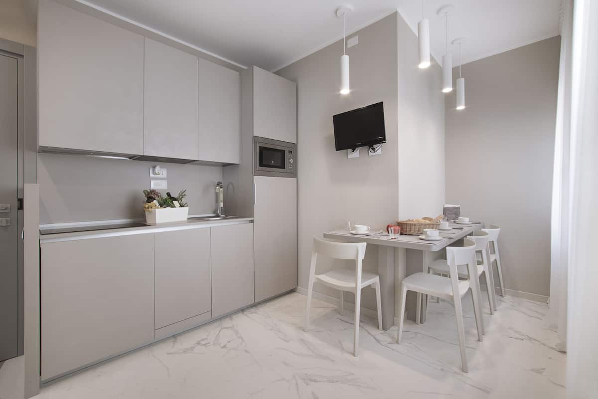 A modern kitchen with grey cabinets, a built-in microwave, and a dining area with white chairs and a table.