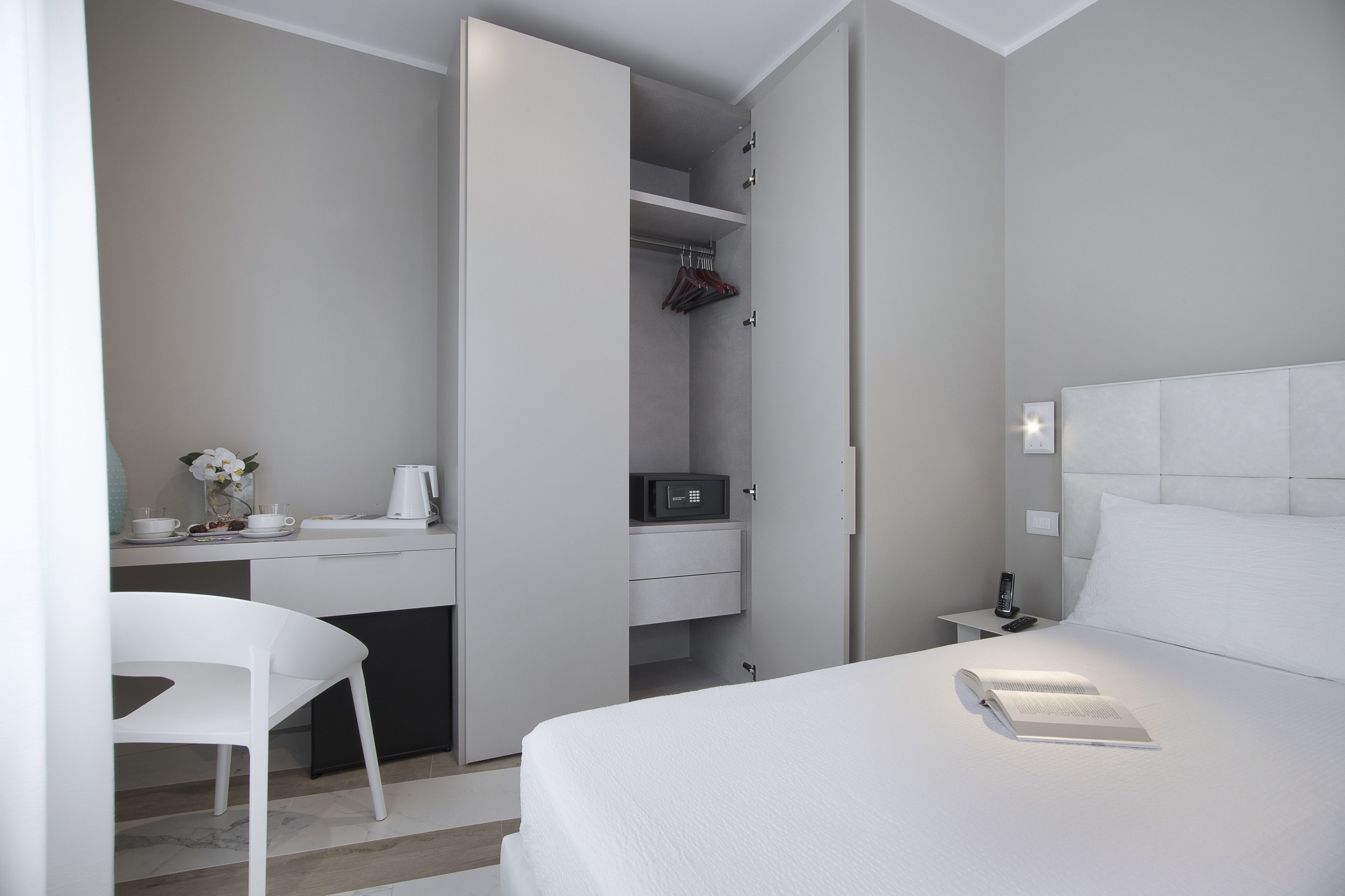 A modern hotel room with a bed, a desk with a chair, a microwave, and a wardrobe.