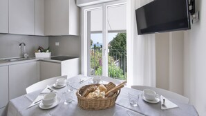Une cuisine moderne avec des meubles blancs, une table à manger dressée avec de la vaisselle blanche, un panier de pain et un téléviseur fixé au mur.