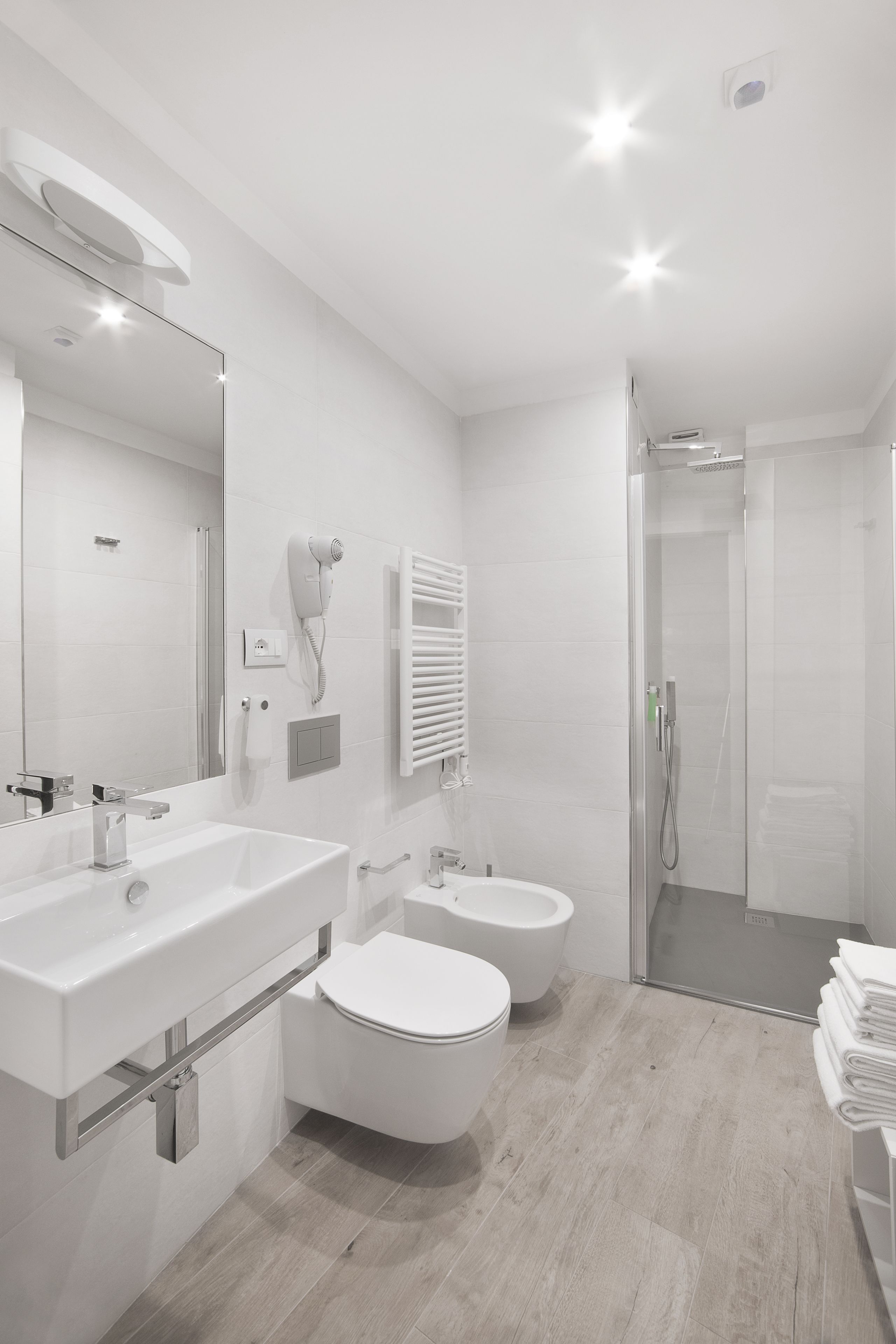 Un baño moderno con un espejo grande, dos lavamanos, un inodoro y una zona de ducha.