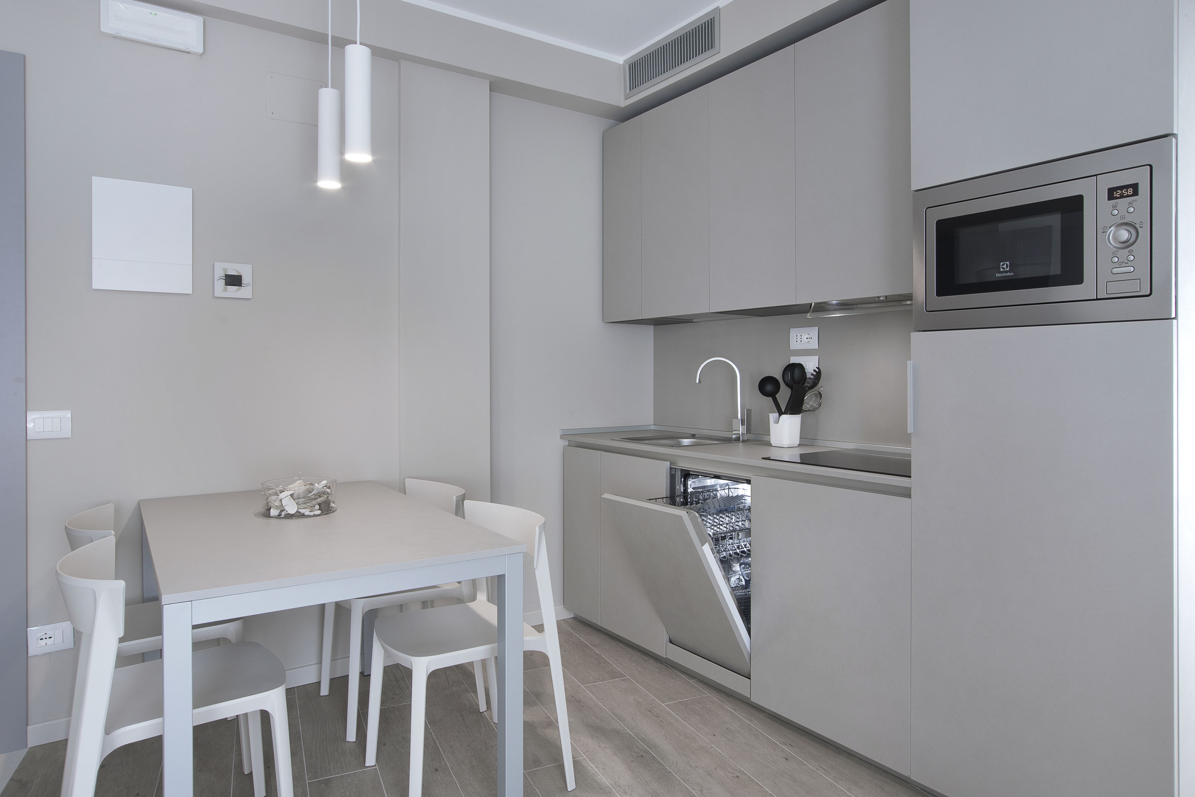 A modern kitchen with a built-in dishwasher, a microwave, and a dining area with white chairs and a table.