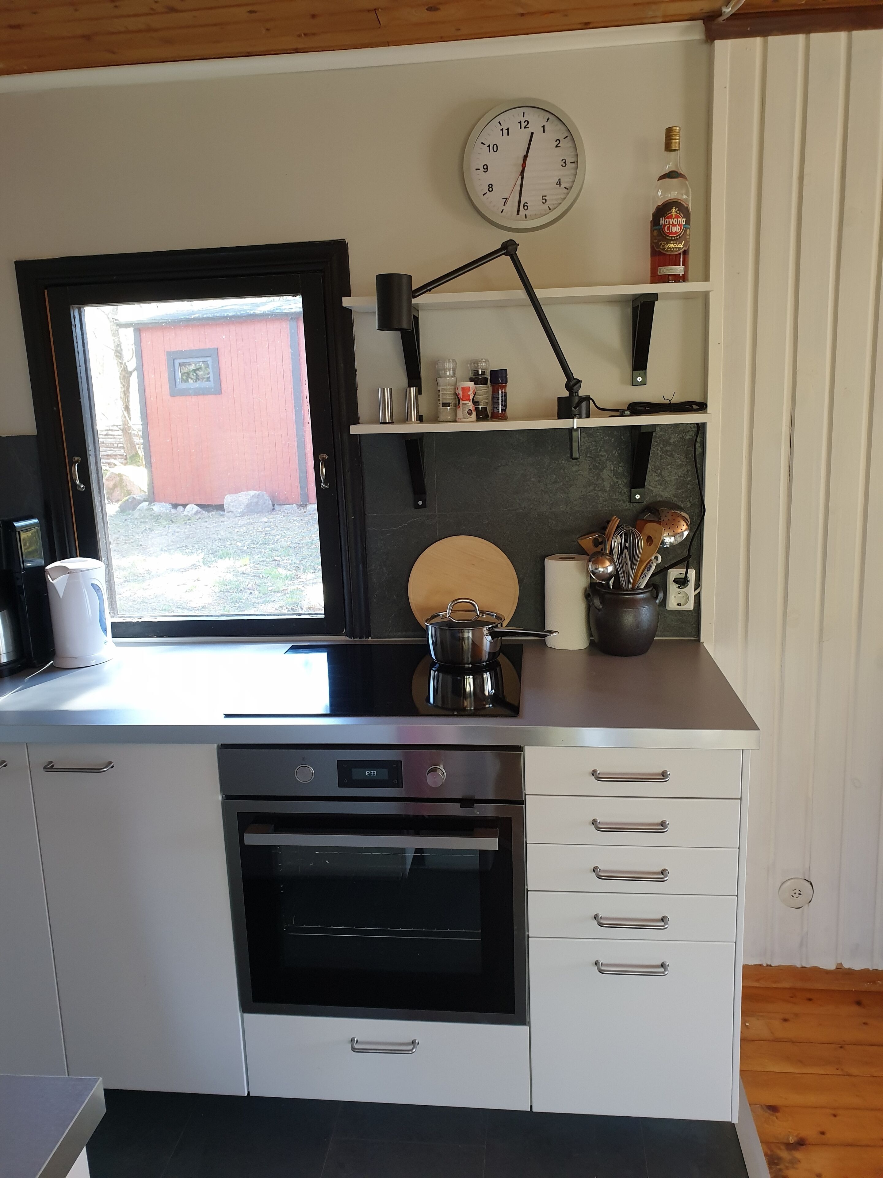 A modern kitchen with a built-in oven, a coffee maker, and a clock on the wall.