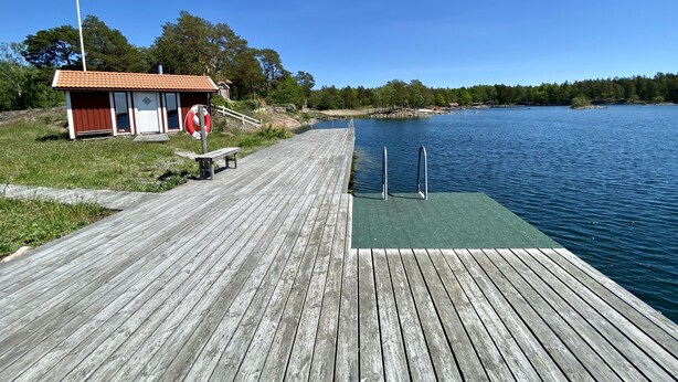 Une jetée en bois mène à un petit bâtiment doté d’un toit rouge, situé au bord d’un lac paisible.